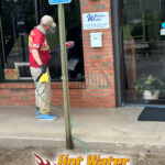 A worker is cleaning the storefront windows of Window World of Tallahassee using a hybrid brush attached to a water-fed pole. The windows are being rinsed with deionized (DI) water.