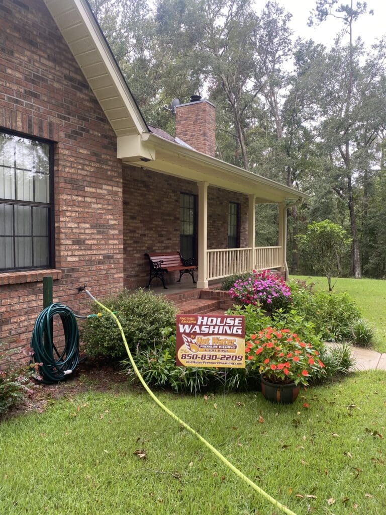 A house washing sign placed in front of a clean, freshly washed front porch. The porch is surrounded by colorful flowers.