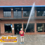 A worker is using a soft wash system to clean the exterior of a two-story commercial office building in Tallahassee, FL.