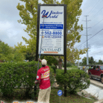 A worker uses a water-fed pole to clean the large "Window World of Tallahassee" sign in front of their office building.