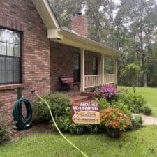 A house washing sign placed in front of a clean, freshly washed front porch. The porch is surrounded by colorful flowers.