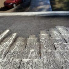 A super close-up image of soft washing soap breaking down algae on a shingled roof.